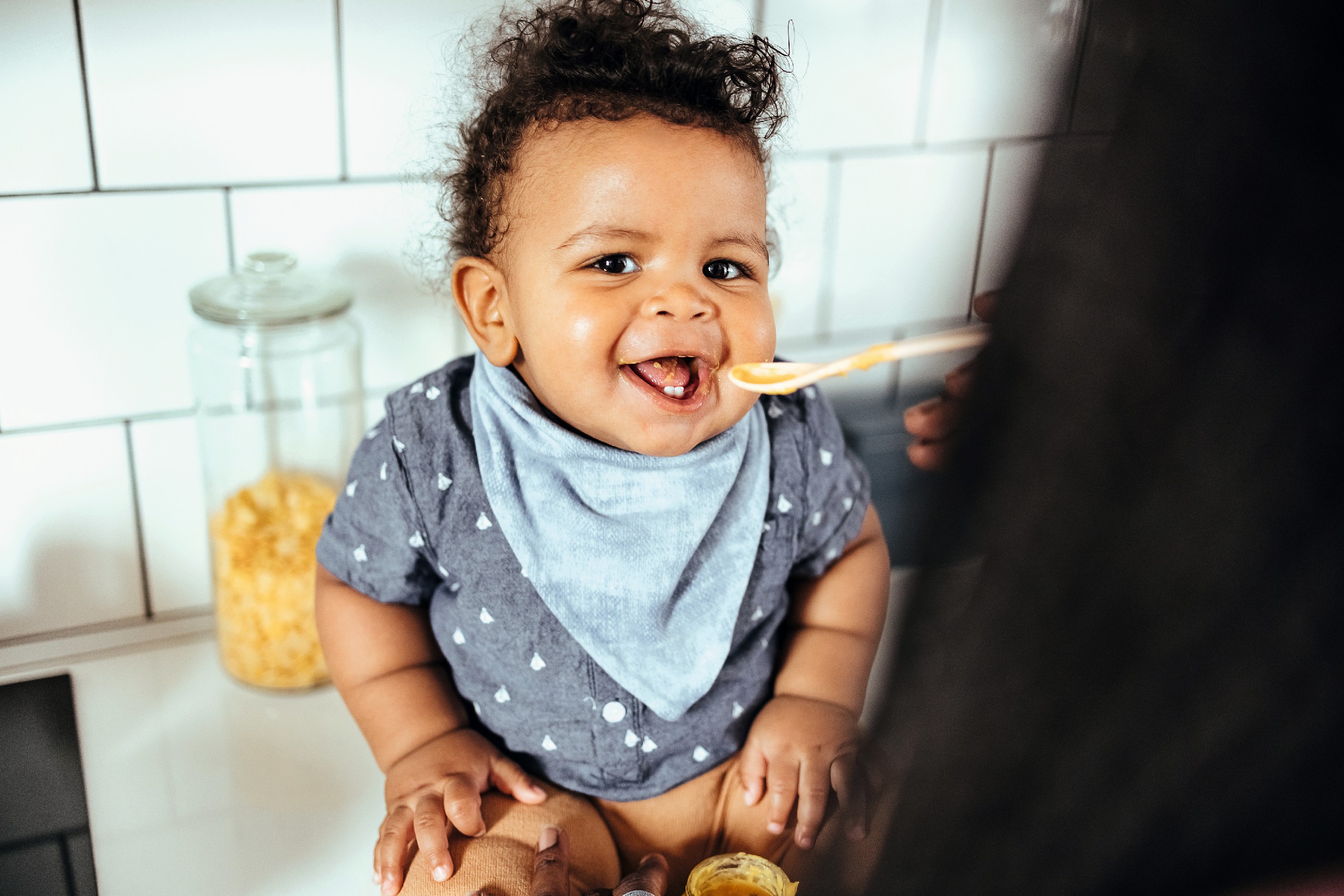 Beautiful mother feeding her baby porridge in the kitchen at home Beautiful mother feeding her baby porridge in the kitchen at home