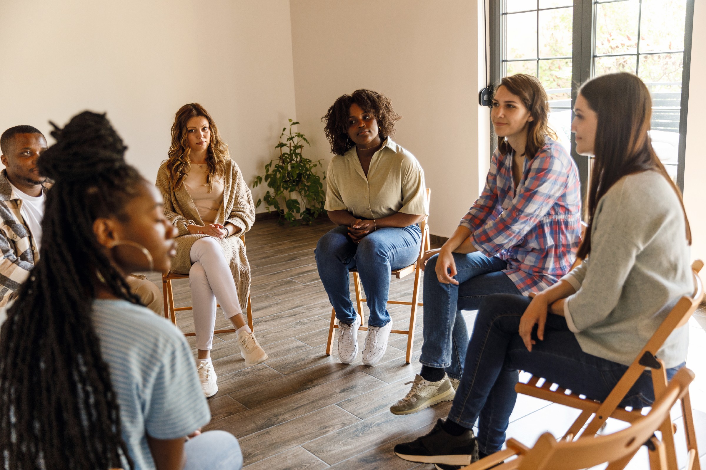 Selective focus shot of diverse group of young people sitting in a circle and talking about their problems during a group therapy session. Selective focus shot of diverse group of young people sitting in a circle and talking about their problems during a group therapy session.